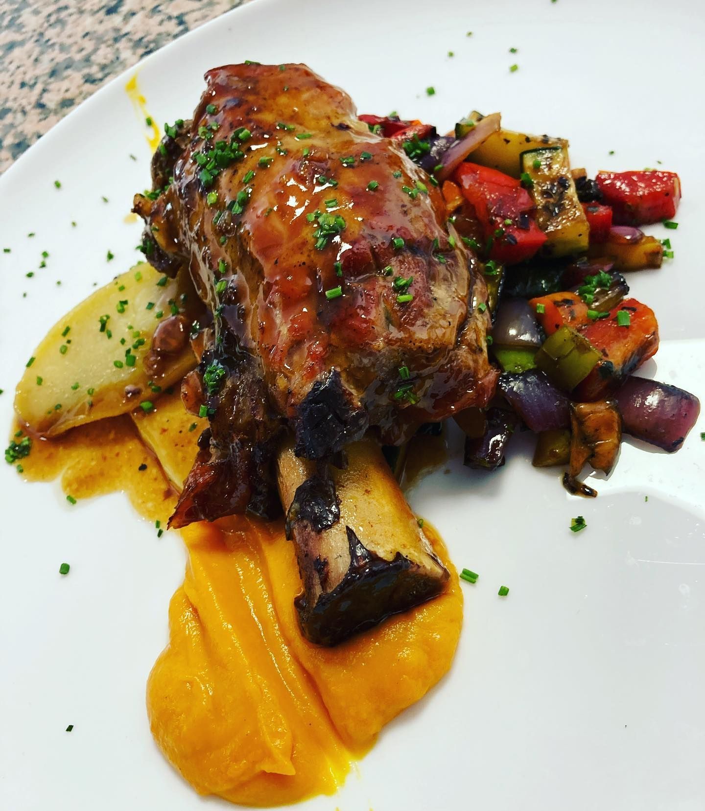 Un plato blanco cubierto con carne, verduras y puré de patatas.