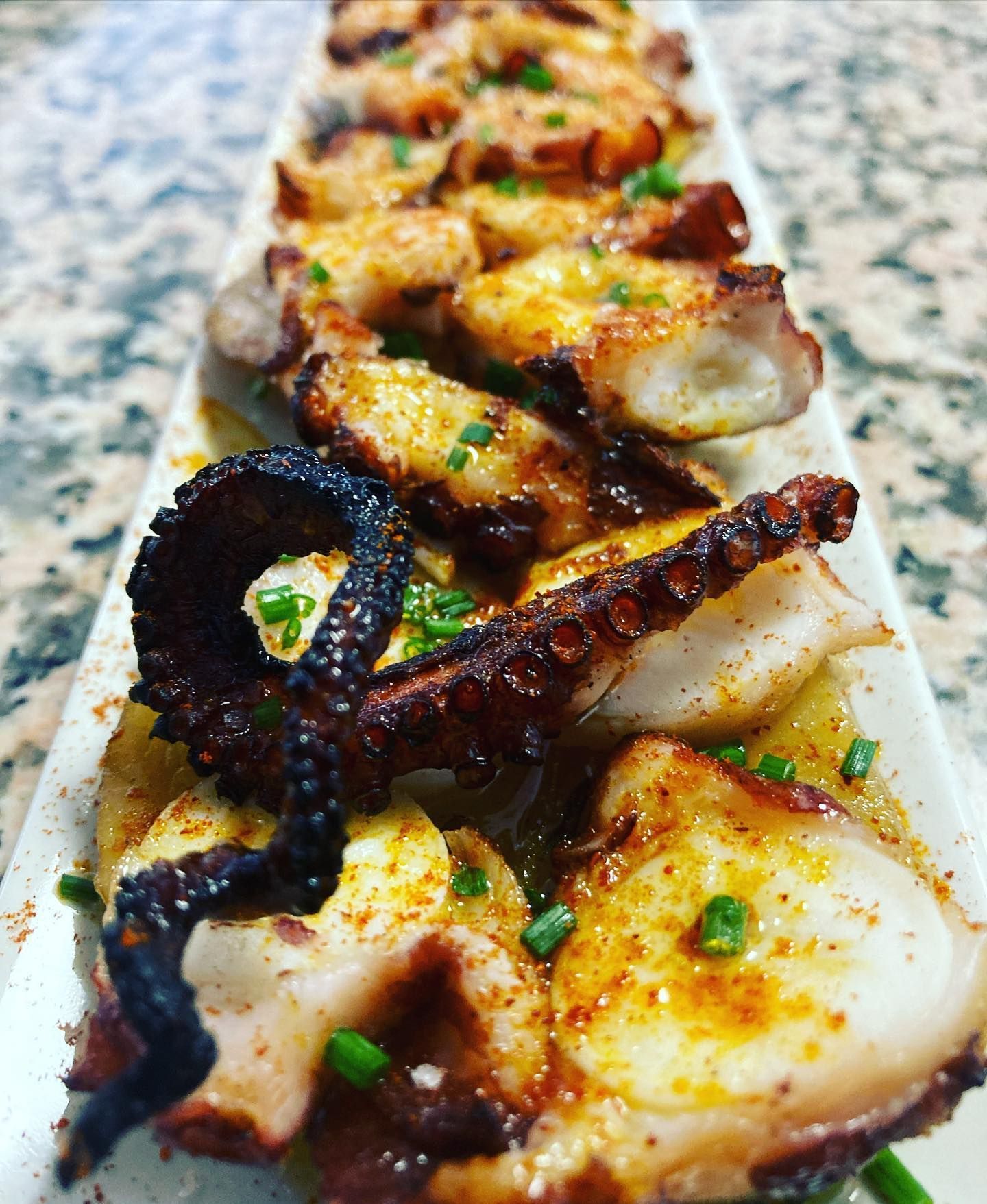 Un plato blanco cubierto con pulpo frito y cebollas verdes sobre una mesa.