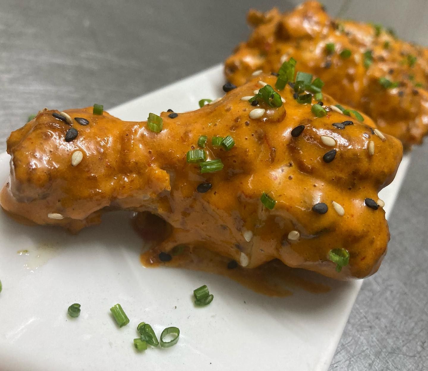 Un plato blanco cubierto con alitas de pollo y salsa.