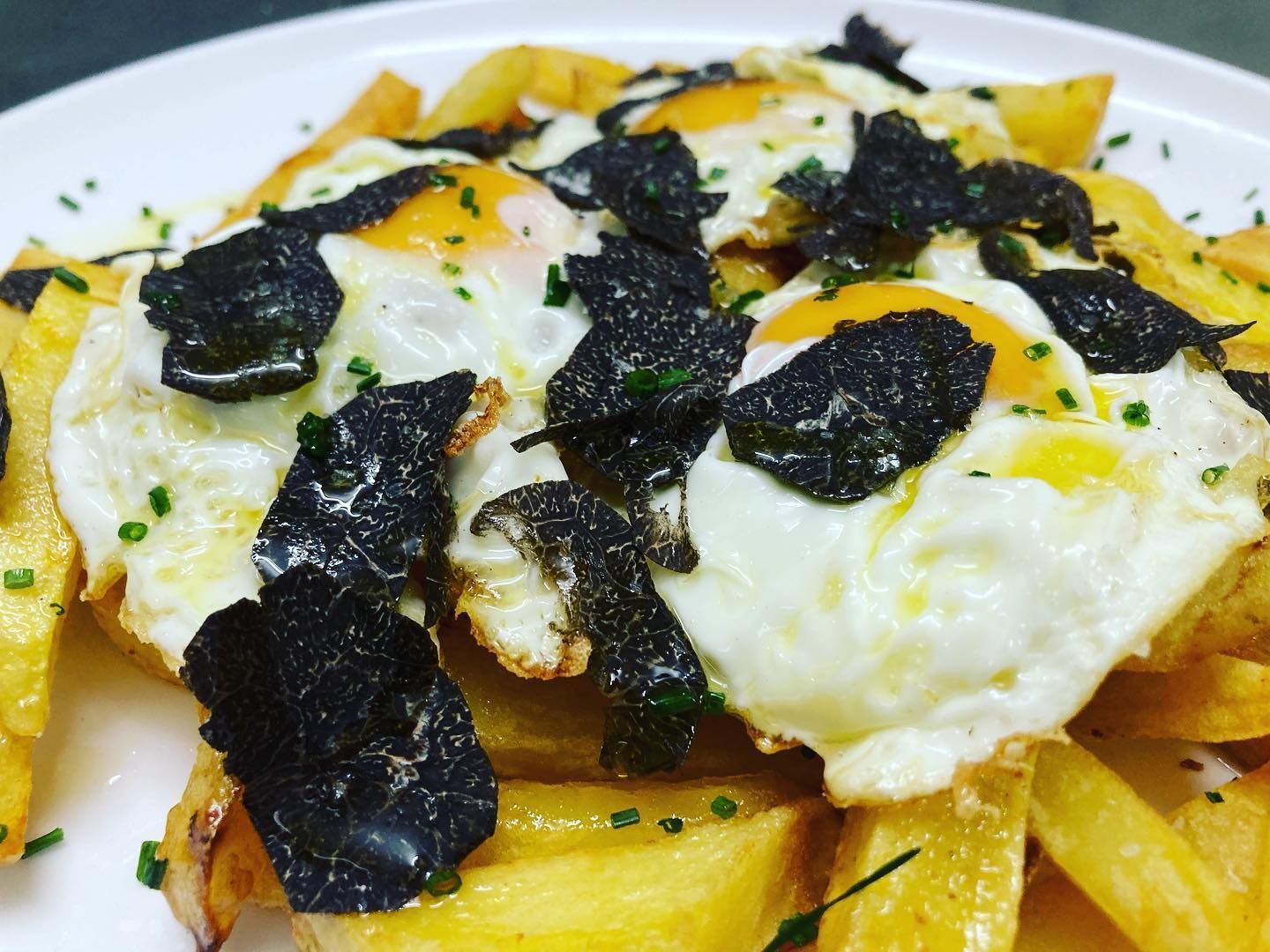 Un plato de patatas fritas con huevos y trufa encima.