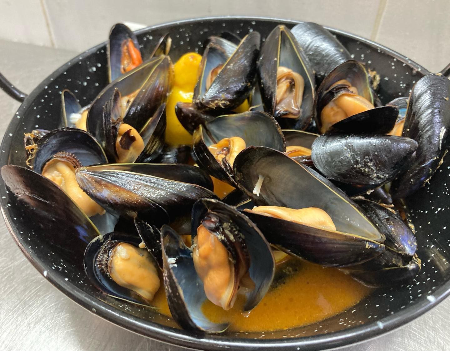 Una sartén llena de mejillones y salsa sobre una mesa.