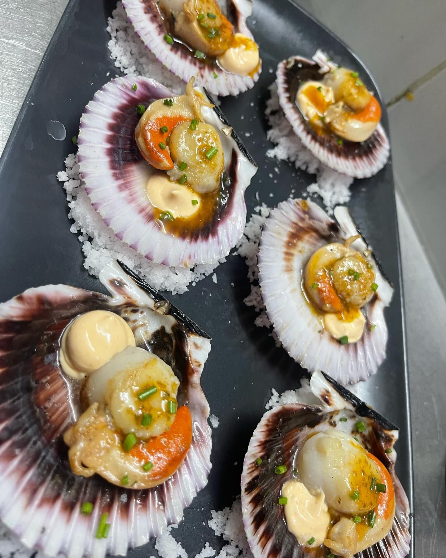 Un plato negro cubierto con vieiras y salsa.