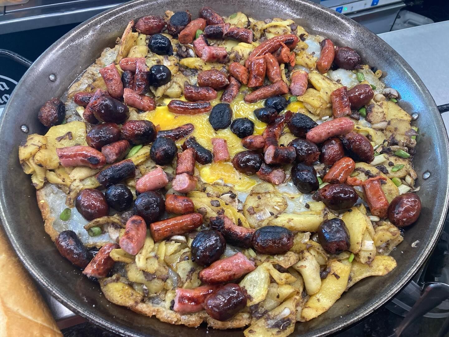 Una sartén llena de mucha comida, incluidas salchichas y aceitunas.