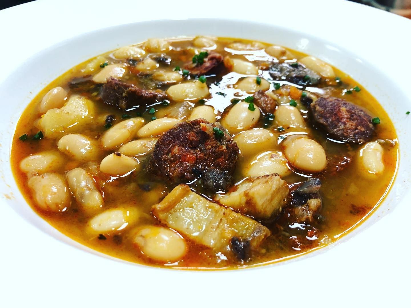 Un tazón de sopa con frijoles y carne en un plato blanco.