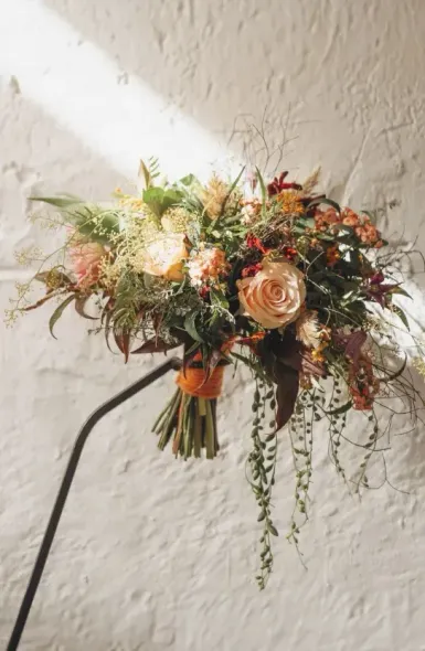 Un ramo de flores reposa sobre una lámpara contra una pared blanca.