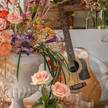 Una guitarra está sobre una mesa al lado de un jarrón de flores.