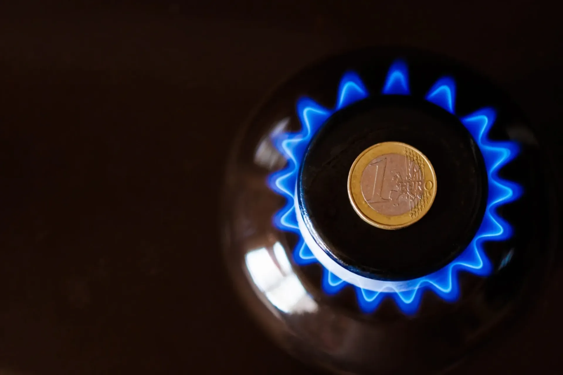 Llama de gas azul alrededor de un quemador de estufa con una tapa de olla encima.