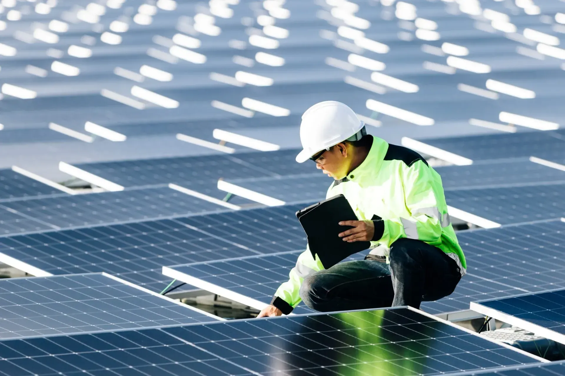 Técnico inspeccionando paneles solares con una tableta en una planta solar.