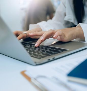 Una mujer está escribiendo en una computadora portátil.