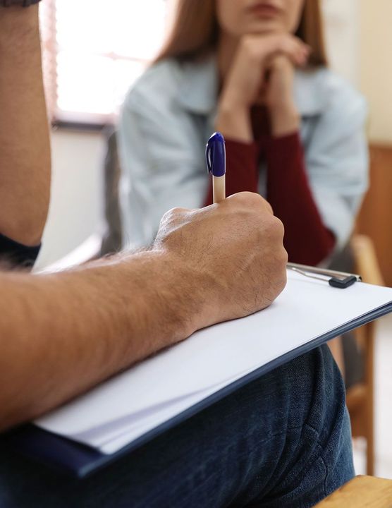 Un hombre está escribiendo en un portapapeles delante de una mujer.