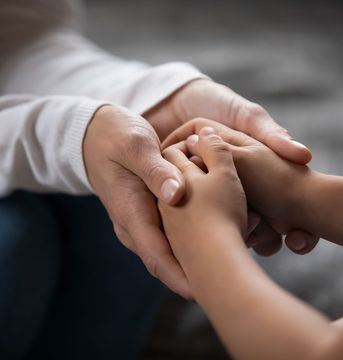 Un primer plano de una persona sosteniendo la mano de un niño.