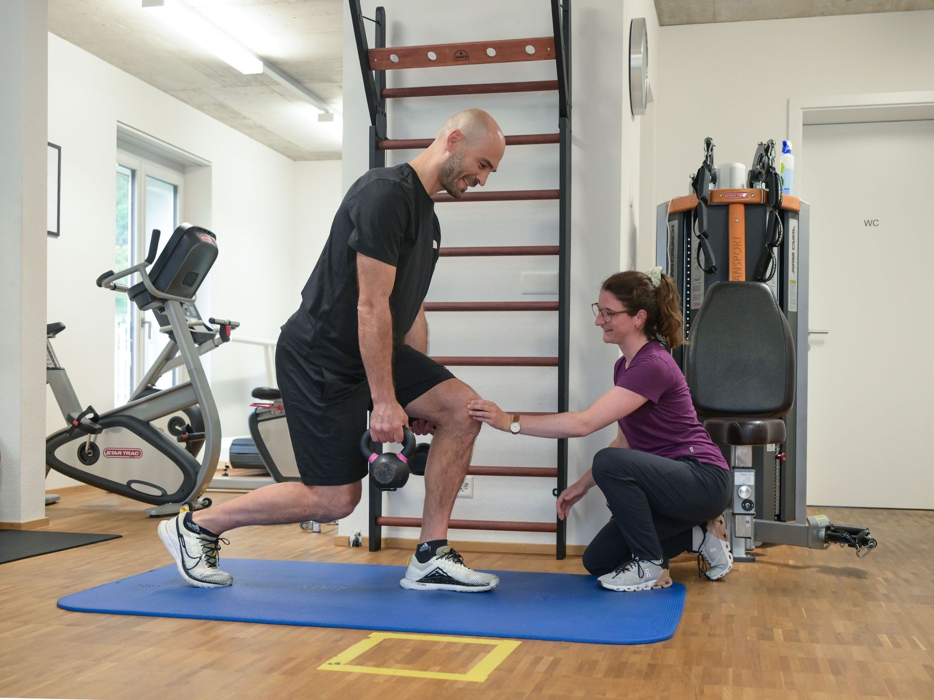 Eine Frau hilft einem Mann in einem Fitnessstudio bei Übungen auf einer Matte.