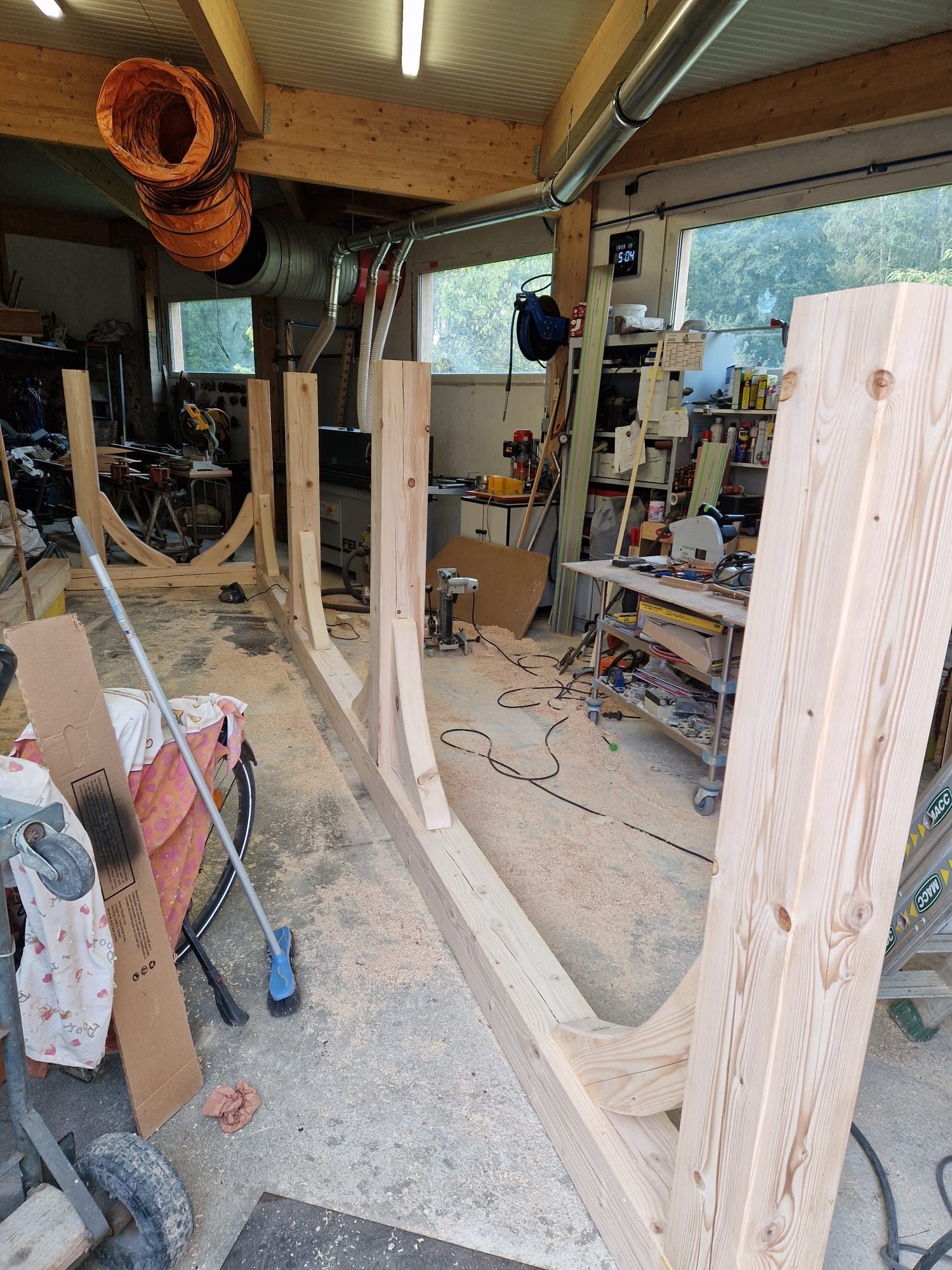 Intérieur d'un atelier avec une grande charpente en bois en construction, des outils et de la sciure de bois au sol.