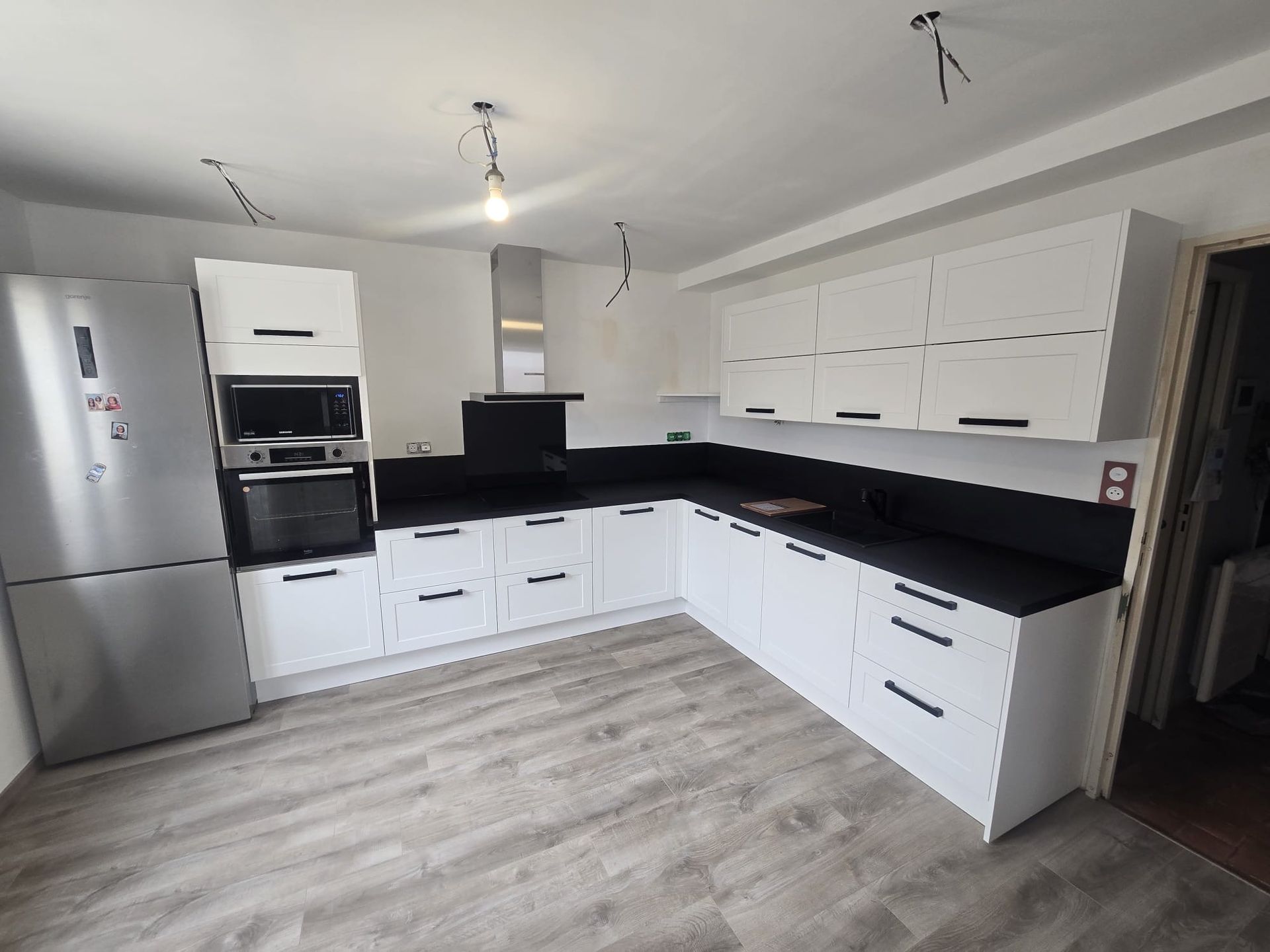 Cuisine moderne blanche avec comptoirs noirs, électroménagers en acier inoxydable et plancher en bois clair.