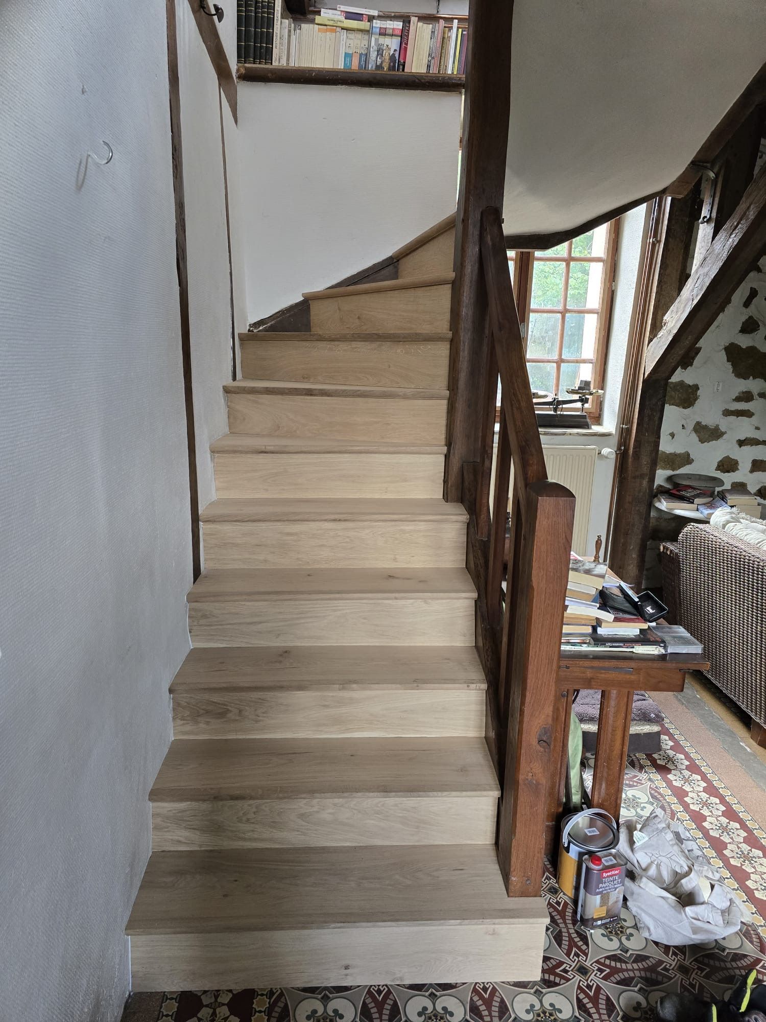 Escalier intérieur avec marches recouvertes de moquette beige et rampe en bois, donnant sur un couloir étroit.