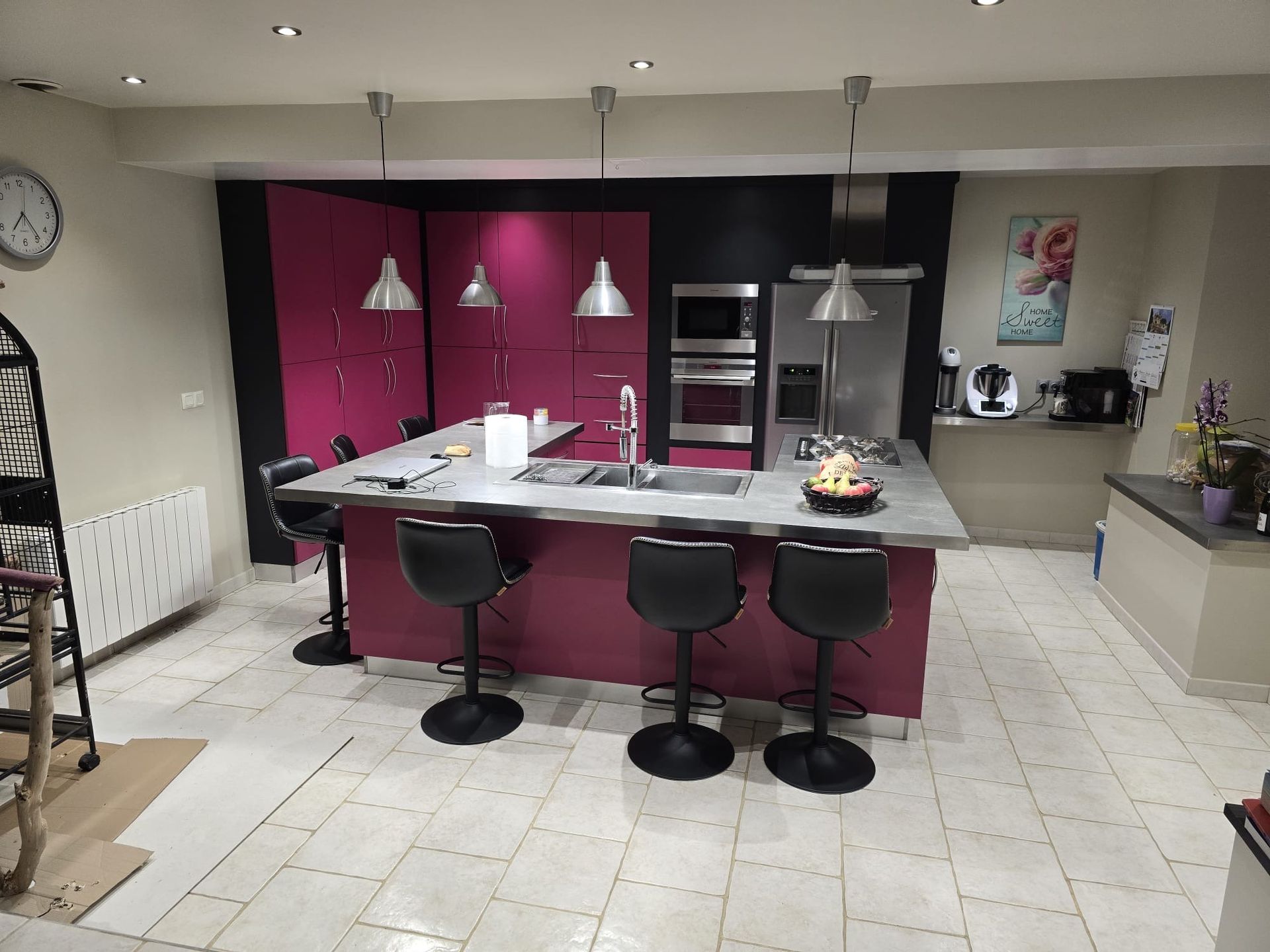 Cuisine moderne avec placards magenta, tabourets de bar sur l'îlot central, suspensions lumineuses et sol carrelé.