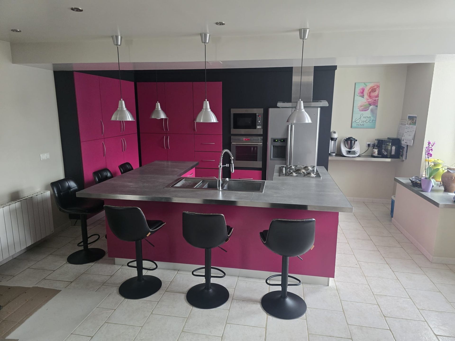 Cuisine moderne avec placards magenta, îlot central et trois tabourets de bar noirs.