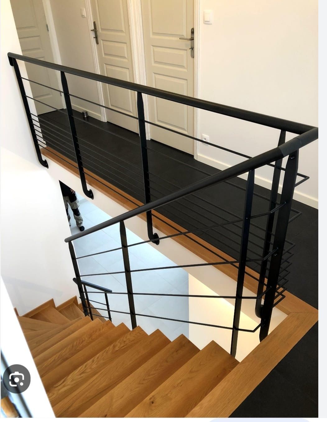 Escalier moderne avec marches en bois, rampe en métal noir et palier à l'étage.