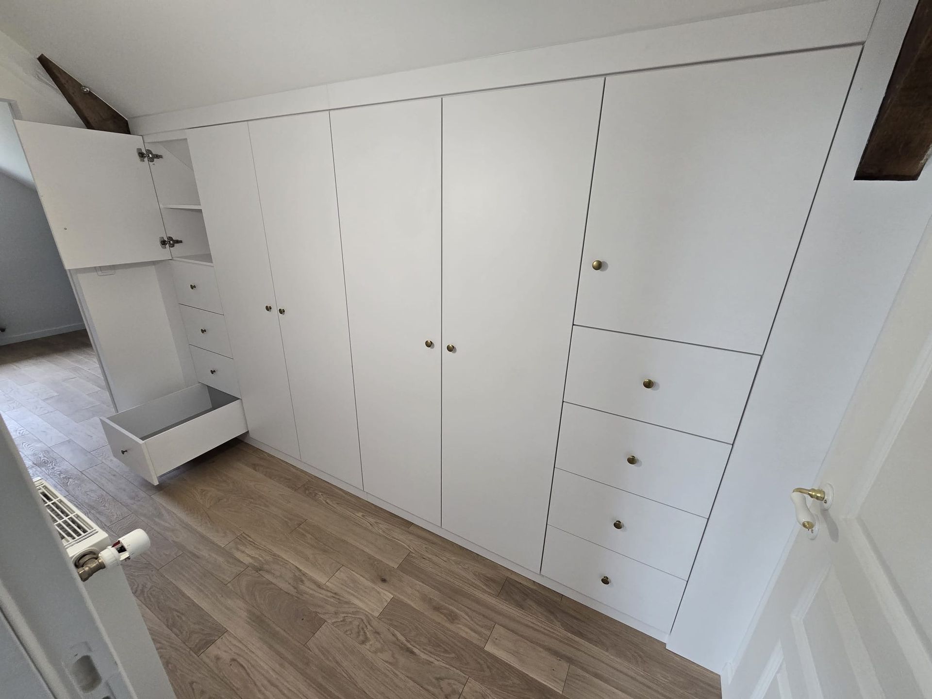 Armoires et tiroirs encastrés blancs dans la chambre, le long d'un mur en pente, avec parquet.