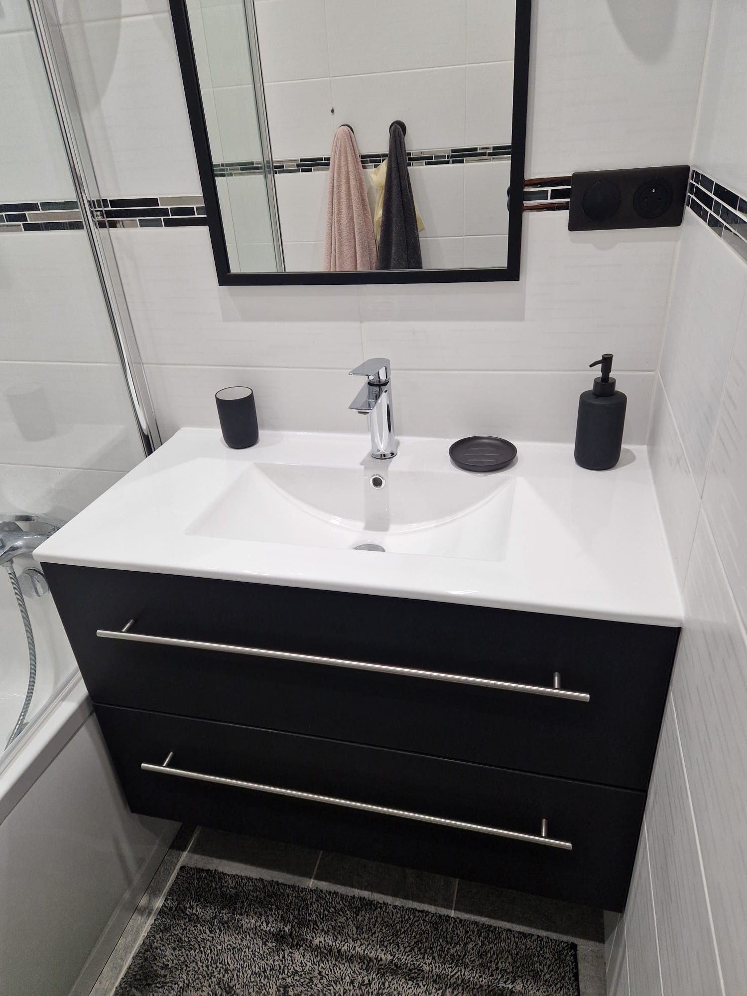 Meuble-lavabo moderne noir et blanc avec lavabo, miroir et douche partiellement visible.