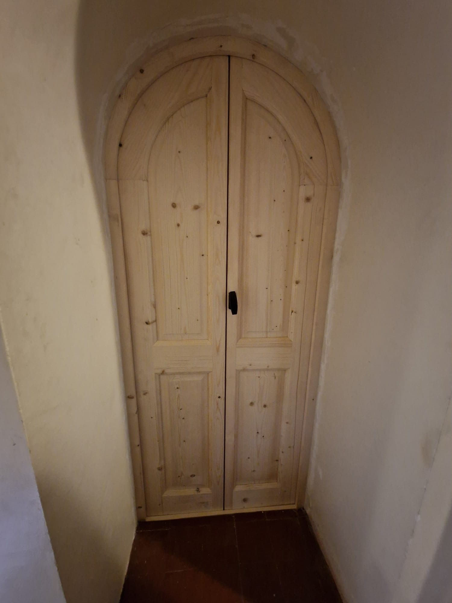 Porte double cintrée en bois avec poignée centrale dans un couloir étroit beige.