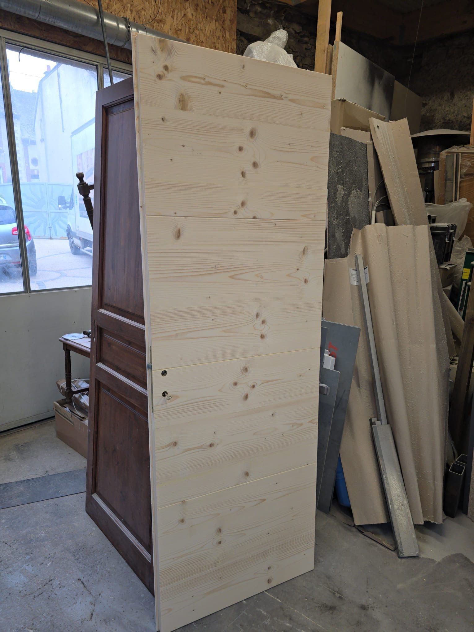 Grand panneau de contreplaqué brut, armoire ou porte, appuyé contre un tas de bois empilé dans un atelier.