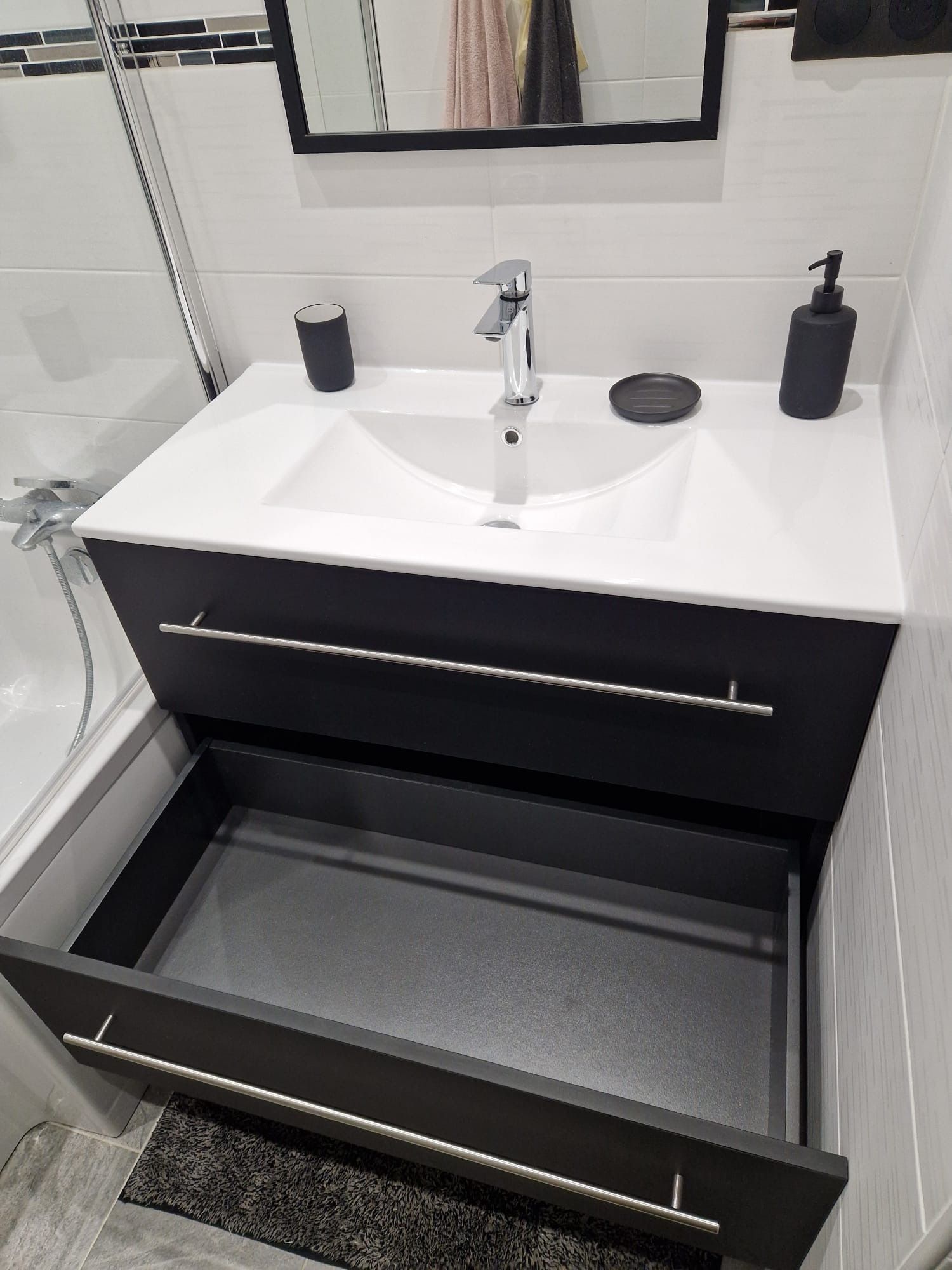 Meuble-lavabo de salle de bain avec lavabo blanc, tiroirs noirs ouverts et articles de toilette sur le comptoir.