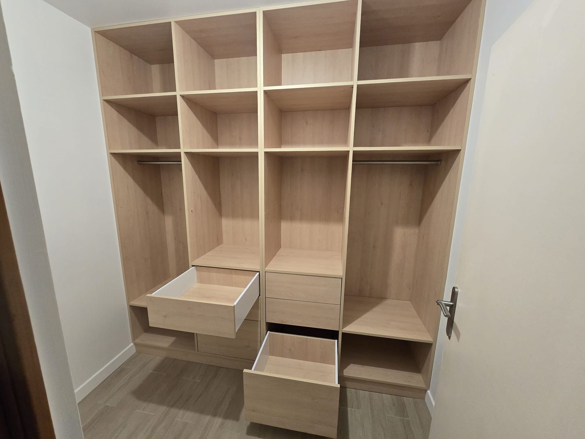 Armoire encastrée en bois avec plusieurs étagères et tiroirs ouverts dans un couloir.