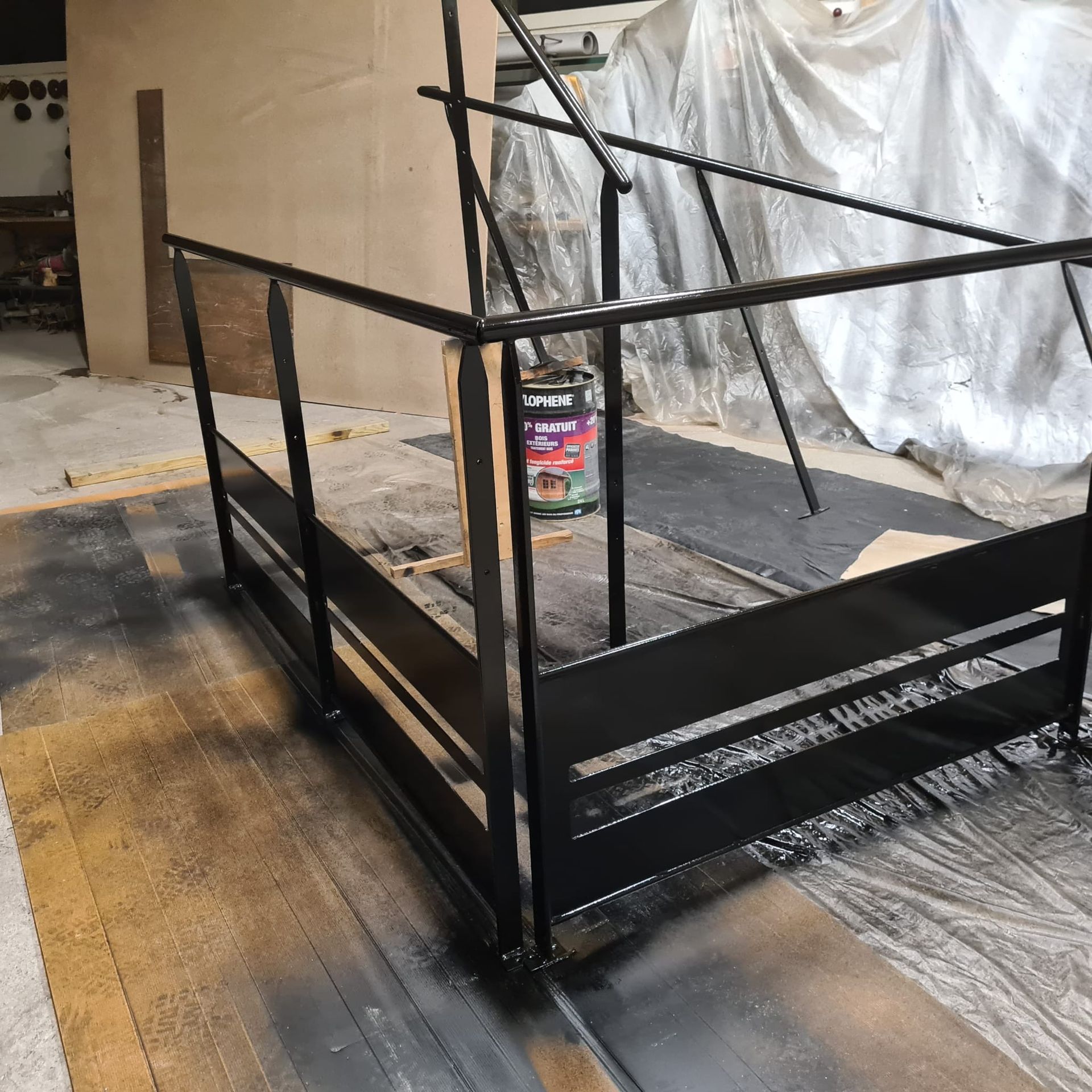Rambardes en métal noir et rampe en construction dans un atelier, avec des bâches en plastique en arrière-plan.