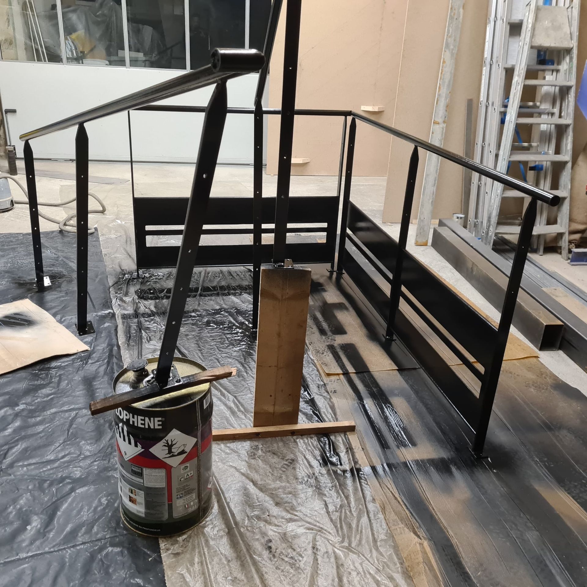 Rambarde en métal noir autour d'une petite rampe en construction, avec un pot de peinture devant.