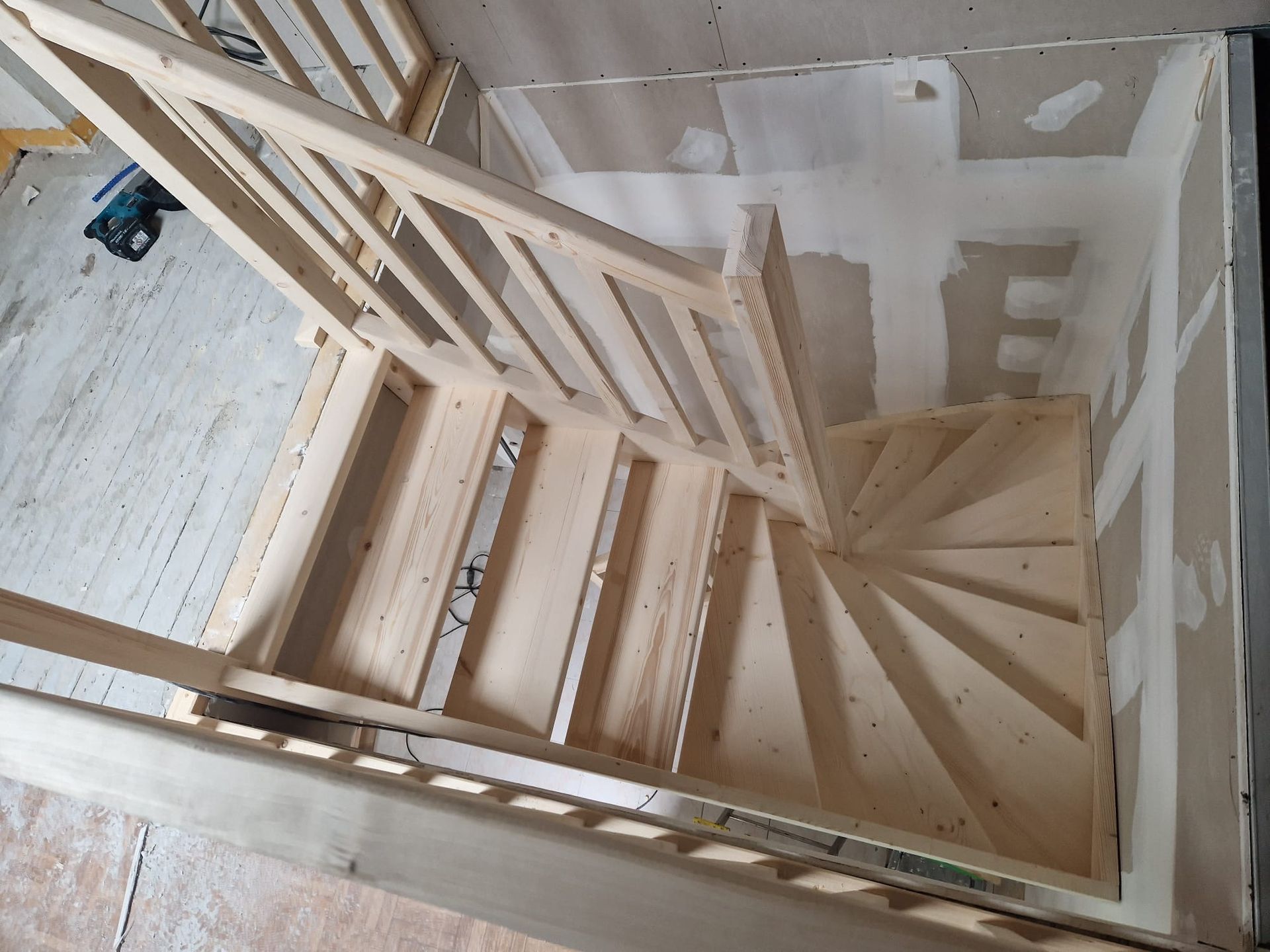 Vue de dessus d'un escalier en bois en construction, avec des murs et des rampes non finis.