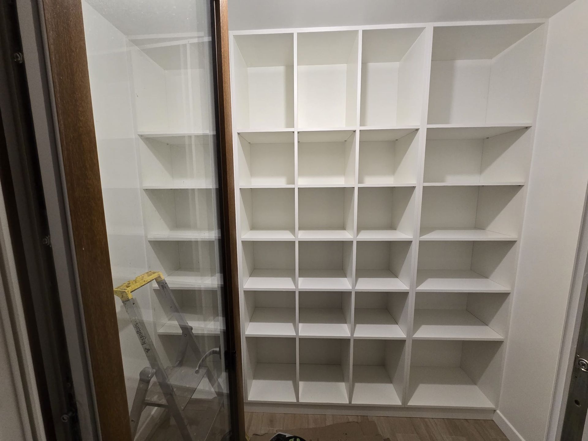Placard intégré blanc avec étagères réglables ; escabeau et outils à gauche lors de l’installation.