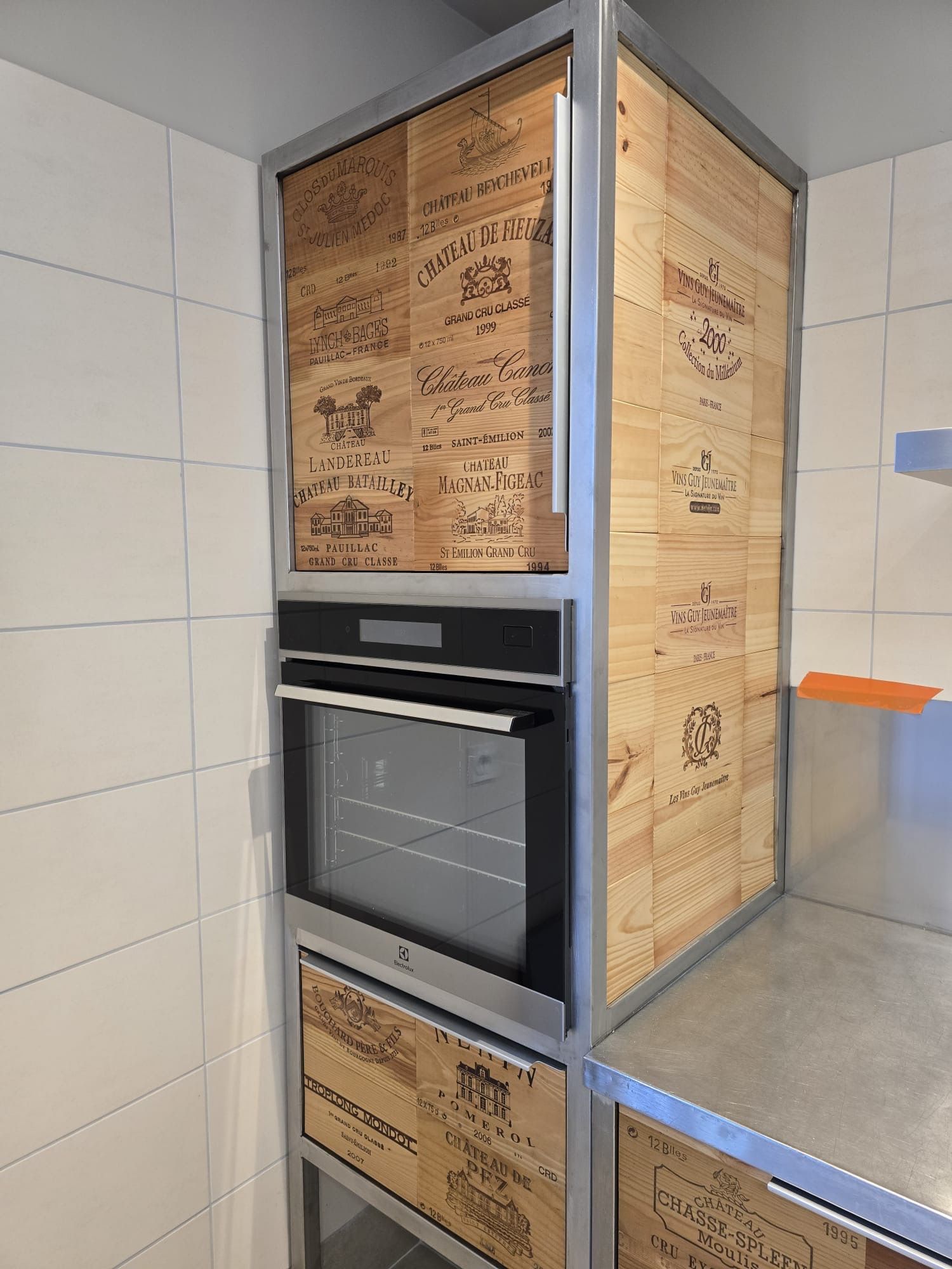 Fours encastrés superposés dans une alcôve carrelée, à côté d'un comptoir en inox et de portes d'armoires à panneaux de bois.