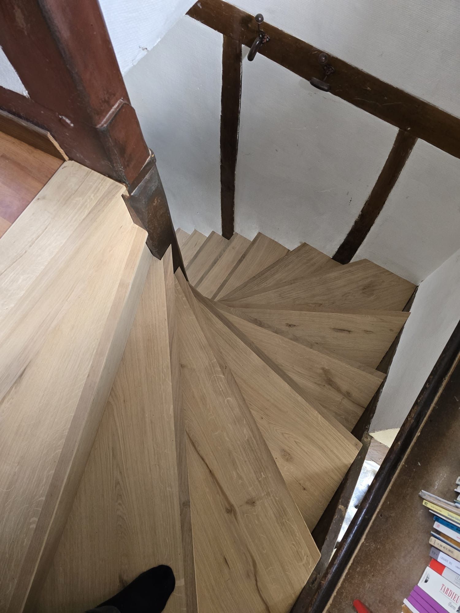 Escalier en bois en colimaçon avec rampe sombre dans une cage d'escalier intérieure étroite, vu d'en haut.