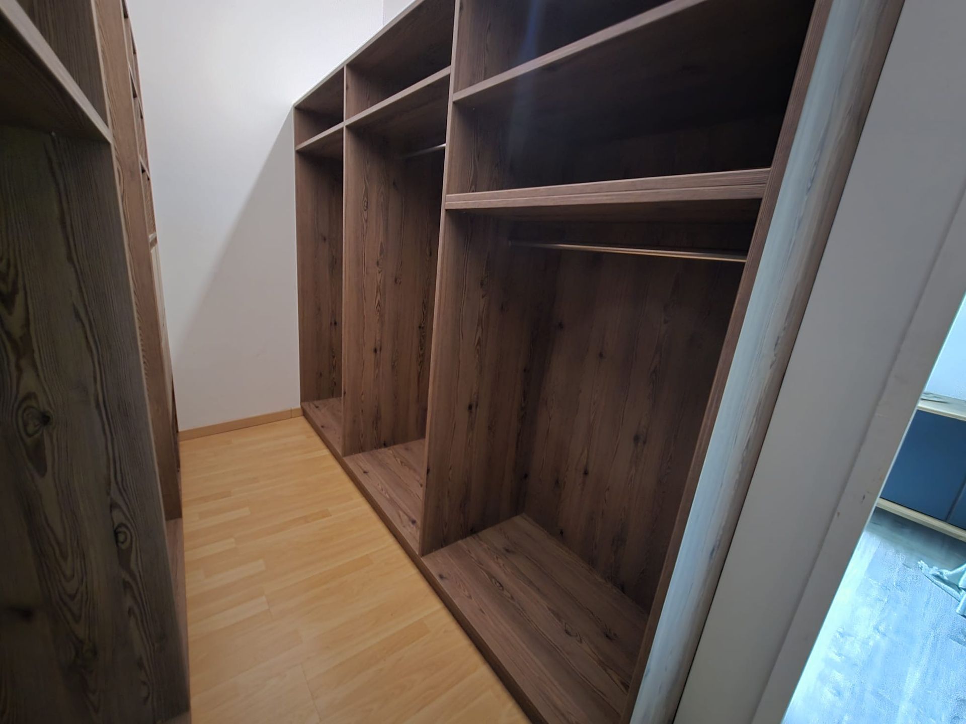 Étagères de placard encastrées en bois le long d'un couloir étroit au parquet clair.