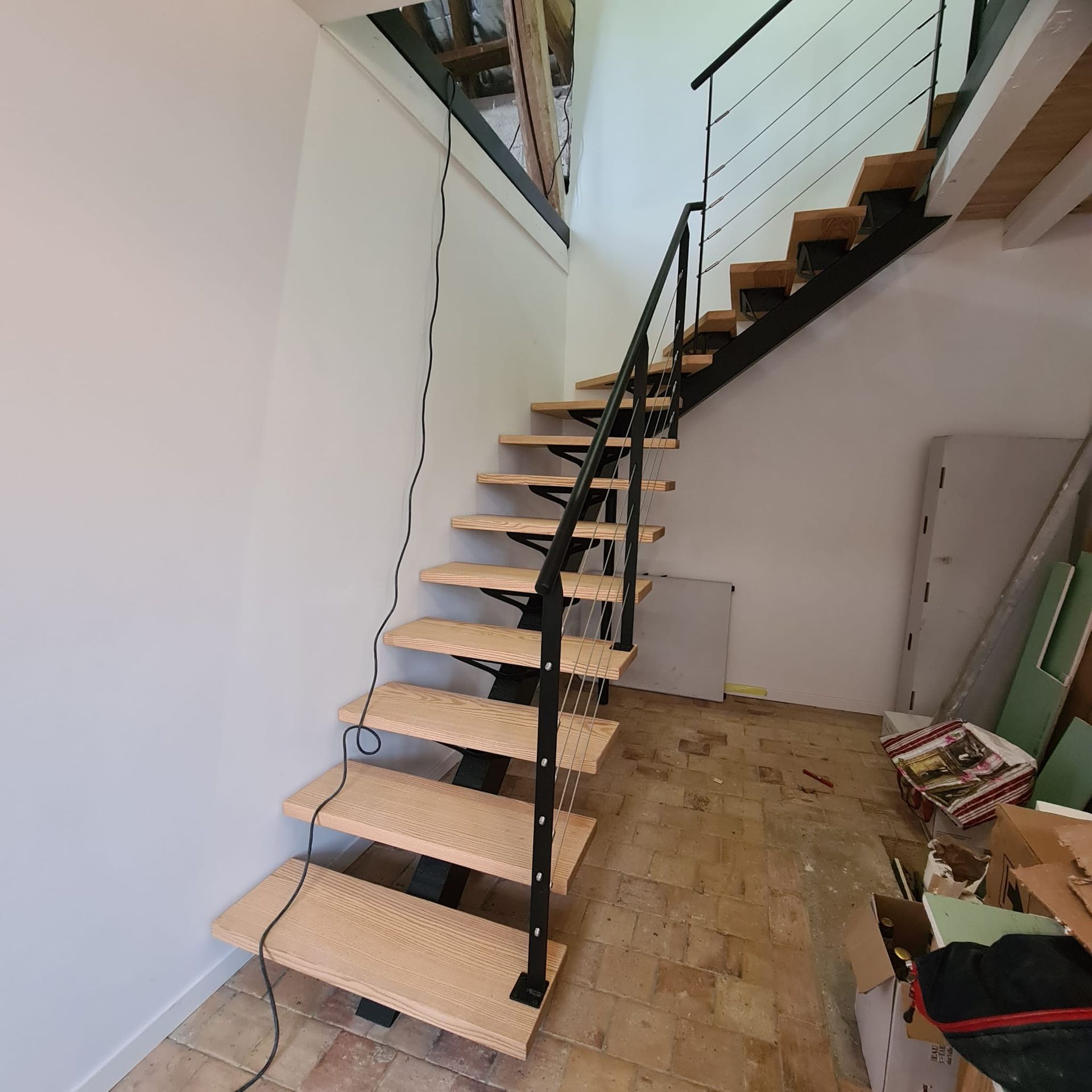 Escalier intérieur avec marches en bois apparentes et rampe noire dans une pièce étroite en construction.