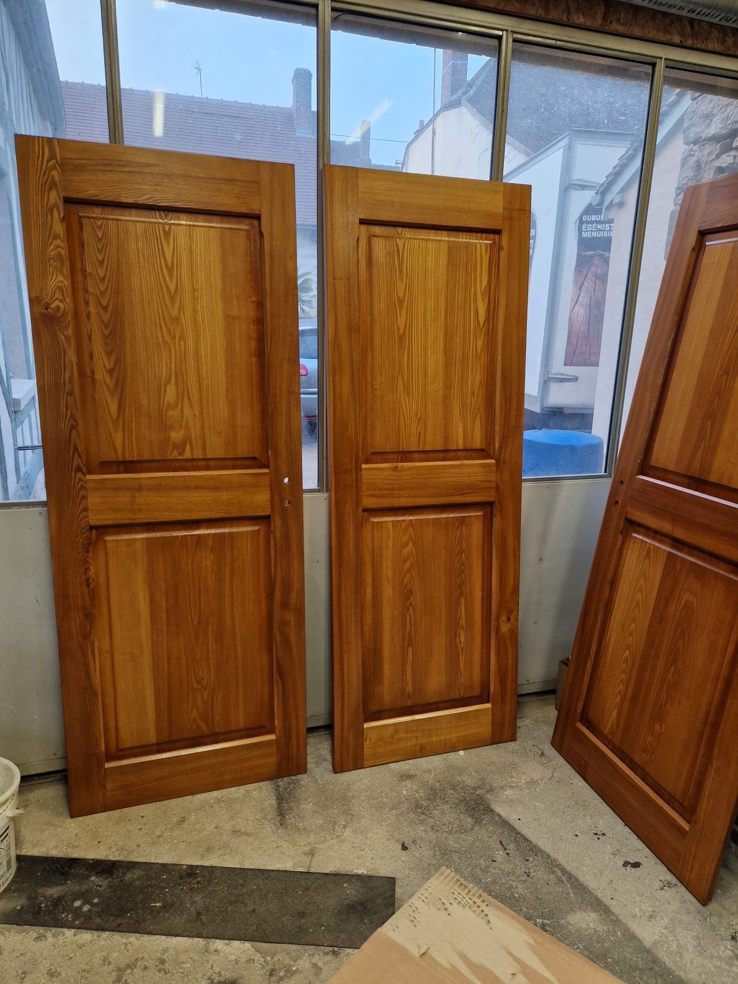 Trois portes d'armoire en bois appuyées contre un mur dans un atelier ou un garage.