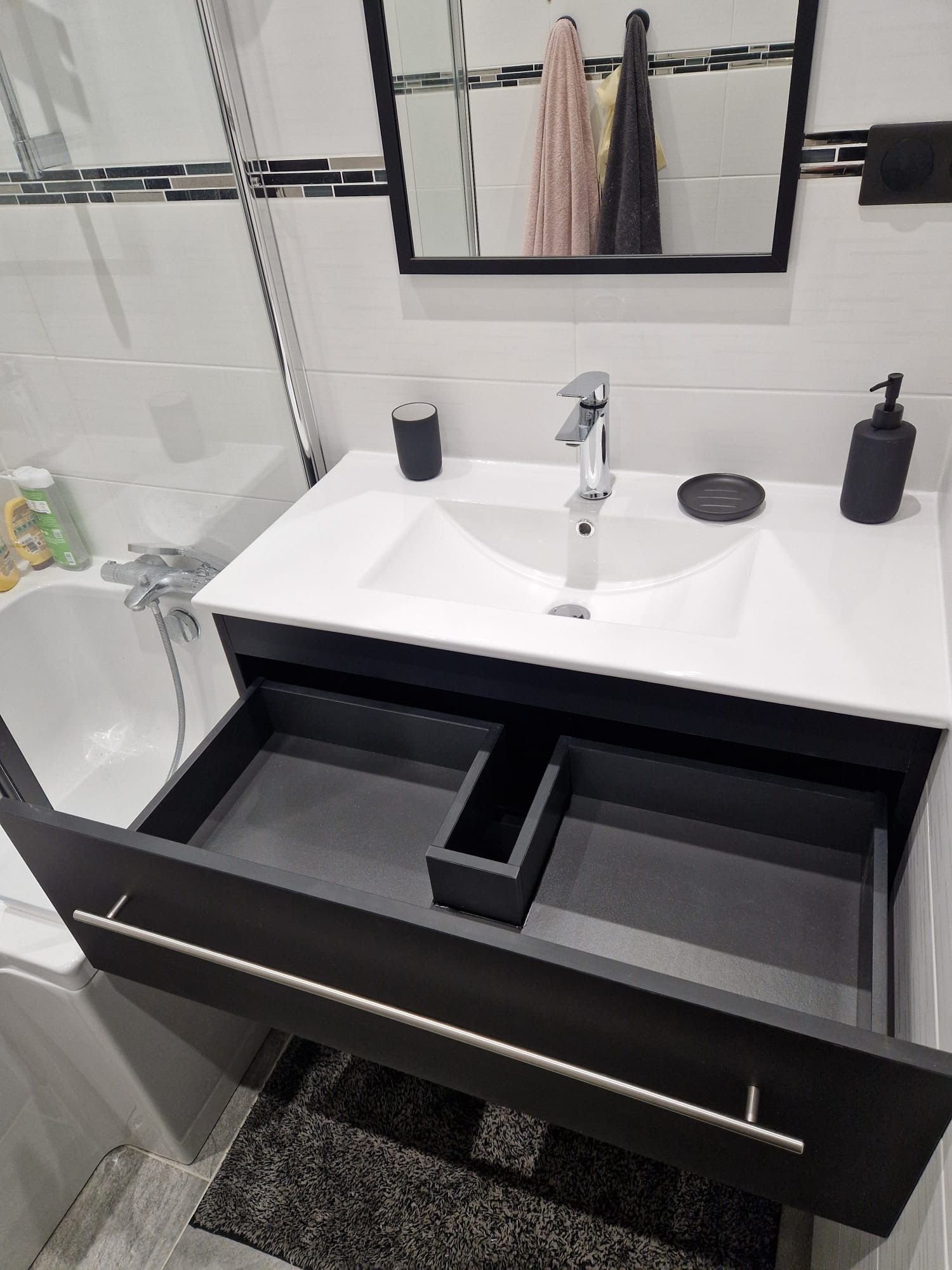 Meuble-lavabo moderne avec tiroirs ouverts, comptoir blanc, miroir et robinetterie noire.