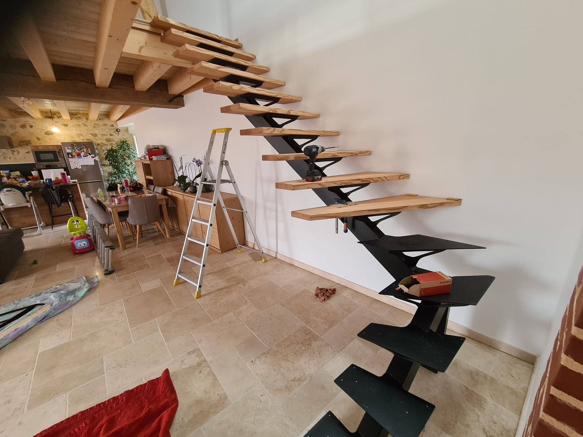 Intérieur avec escalier en bois suspendu et marches en construction, échelle dans une pièce au sol carrelé.