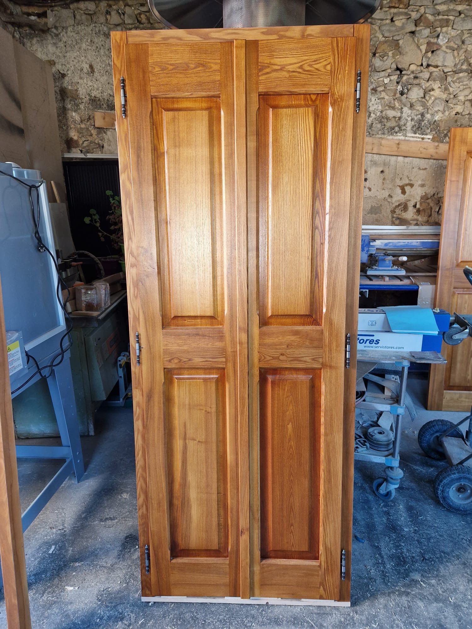 Porte à panneaux en bois couleur miel, placée dans un atelier ou un garage, centrée contre un mur brut.