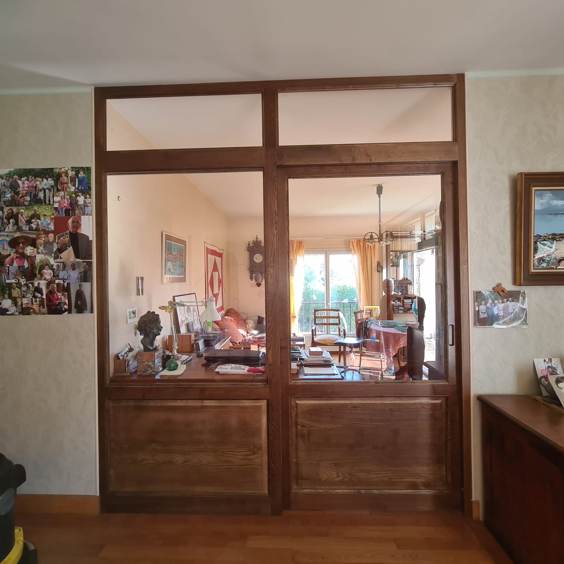 Des portes intérieures vitrées à cadre en bois s'ouvrent sur une salle à manger encombrée, avec une table et un lustre.