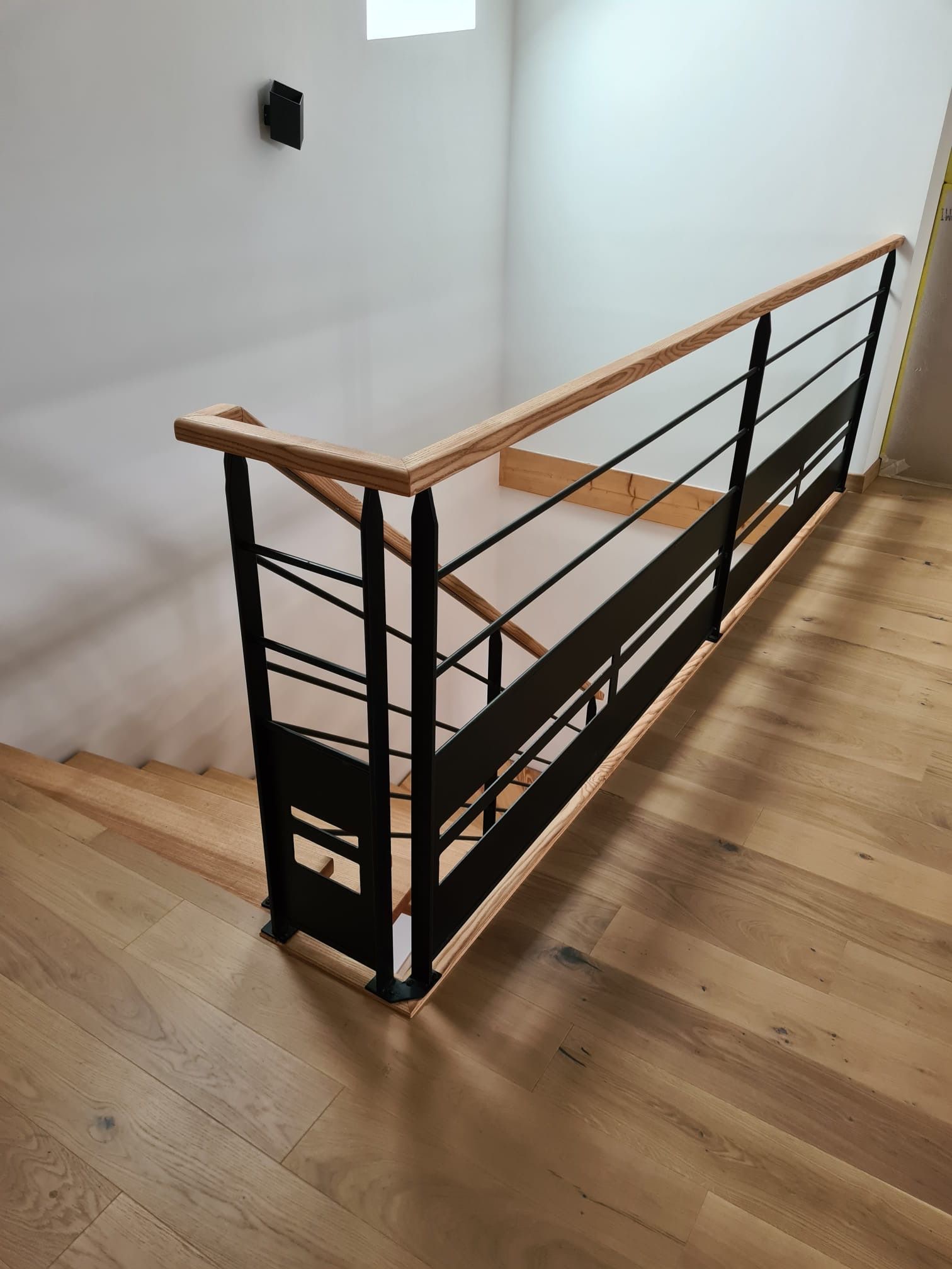 Escalier en bois avec rampe en métal noir dans une pièce intérieure aux murs blancs