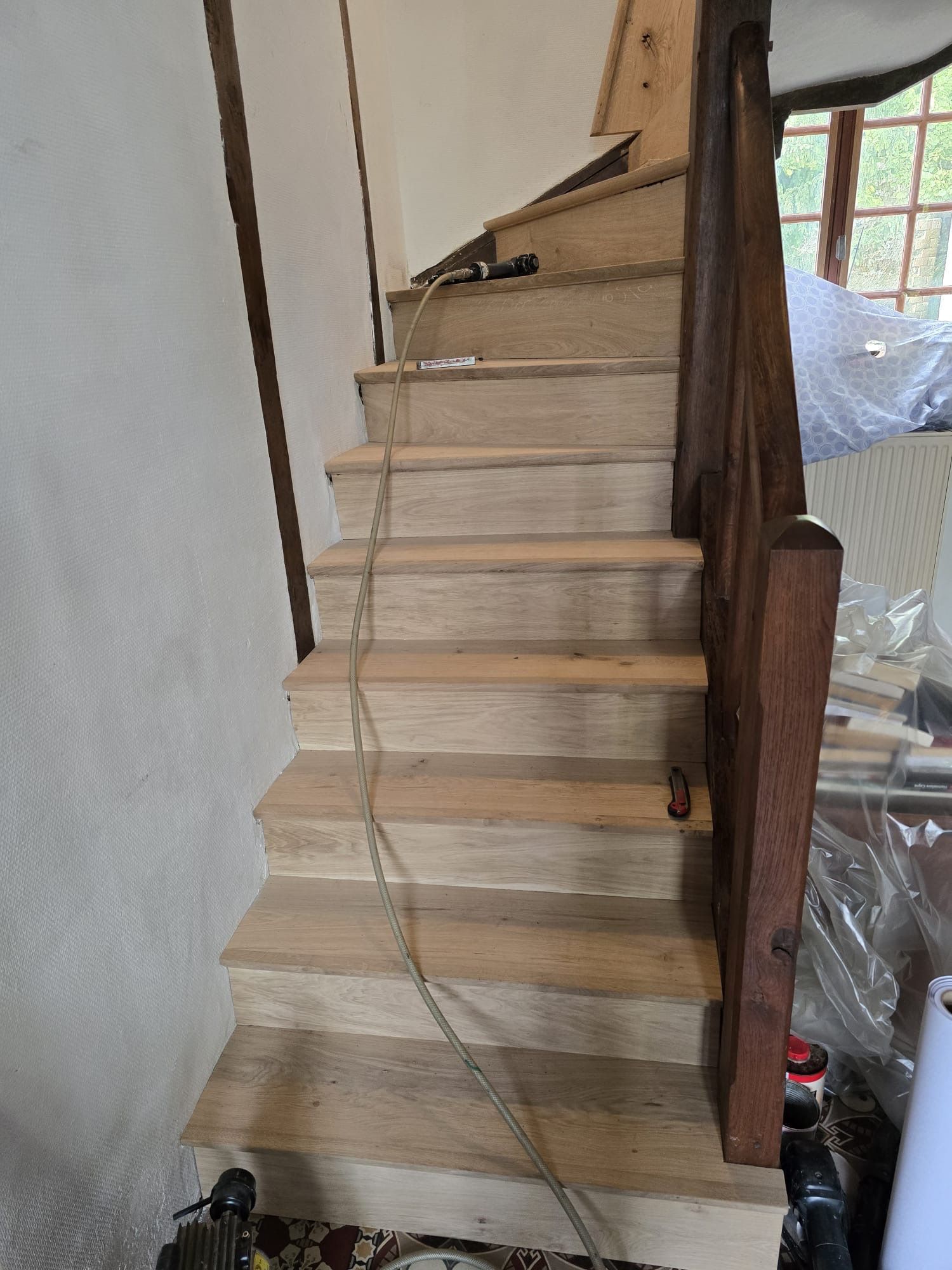 Escalier intérieur étroit en construction, avec marches en bois apparentes et une corde pendant au centre.