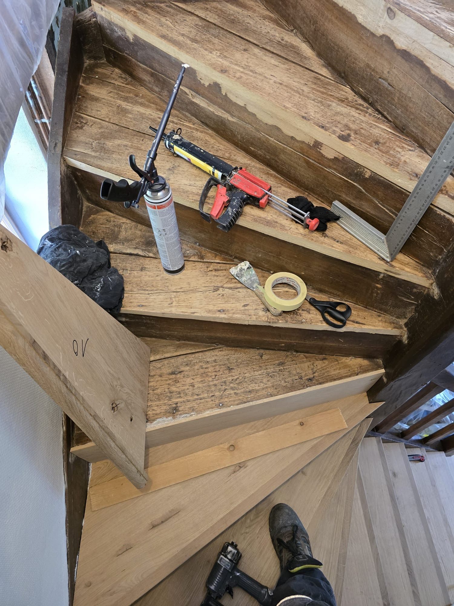 Une personne installe une rampe noire sur un escalier en bois, avec des outils et du ruban adhésif à proximité.