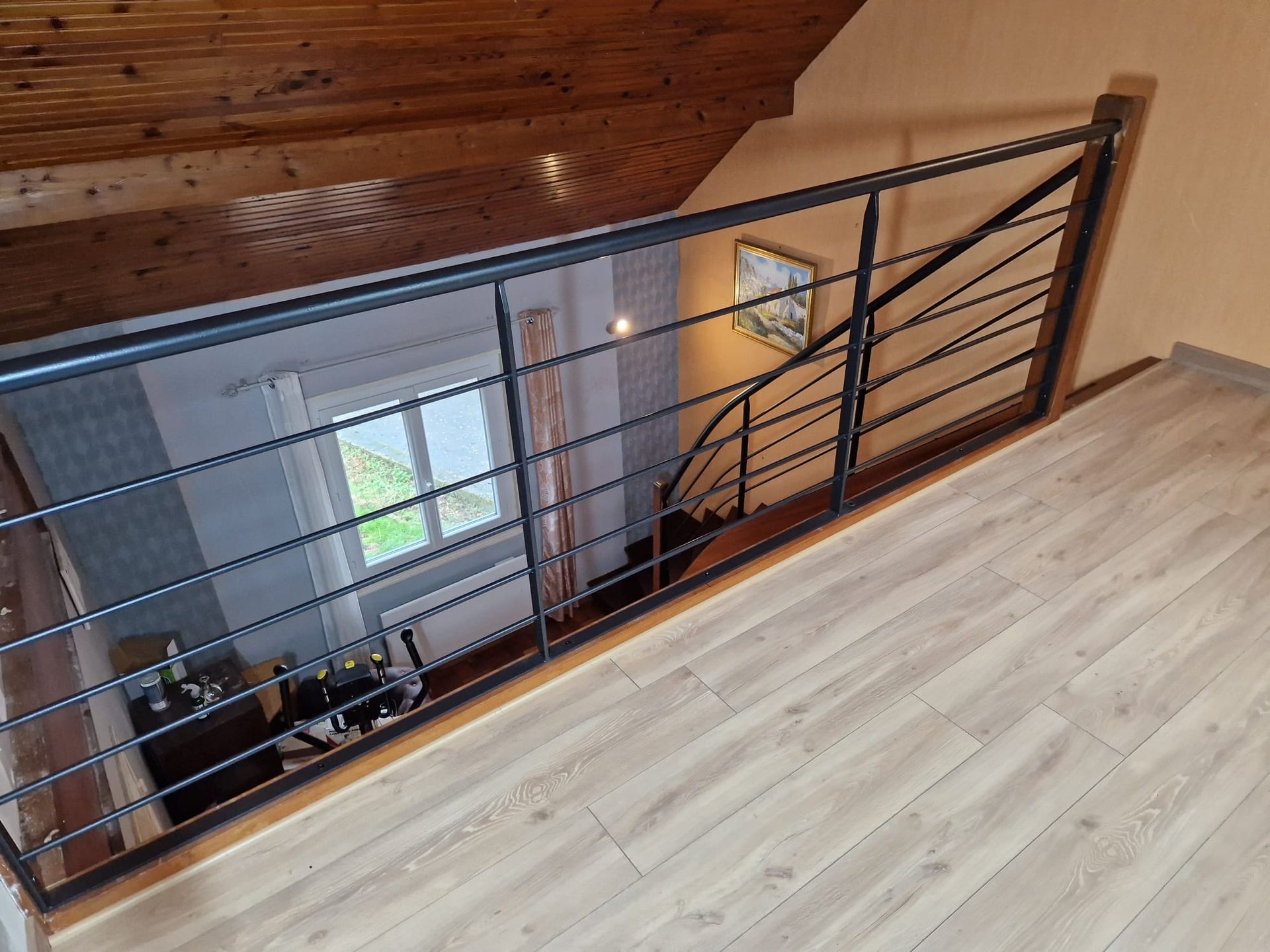 Rambarde de mezzanine avec barres métalliques noires et garnitures en bois donnant sur un étage inférieur et une fenêtre.