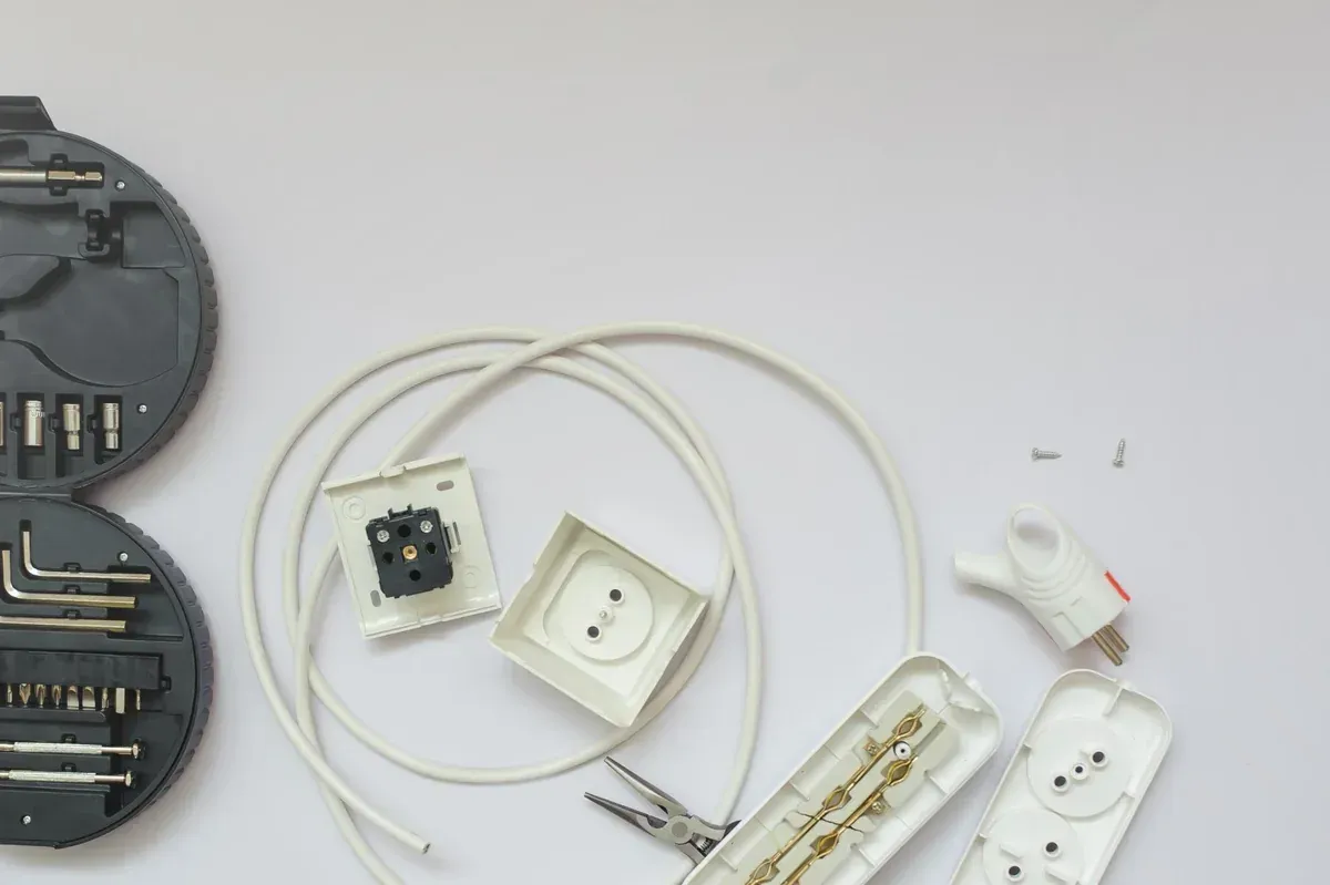 Componentes eléctricos, herramientas y cables desmontados sobre una superficie blanca.