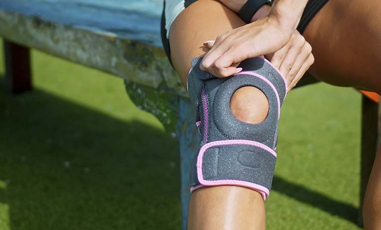 Una mujer lleva una rodillera mientras está sentada en un banco.