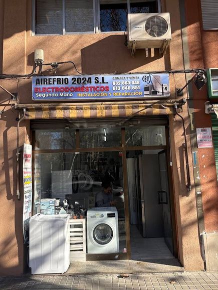Entrada principal de la tienda con electrodomésticos de lavandería expuestos en el exterior y un letrero azul sobre la puerta.