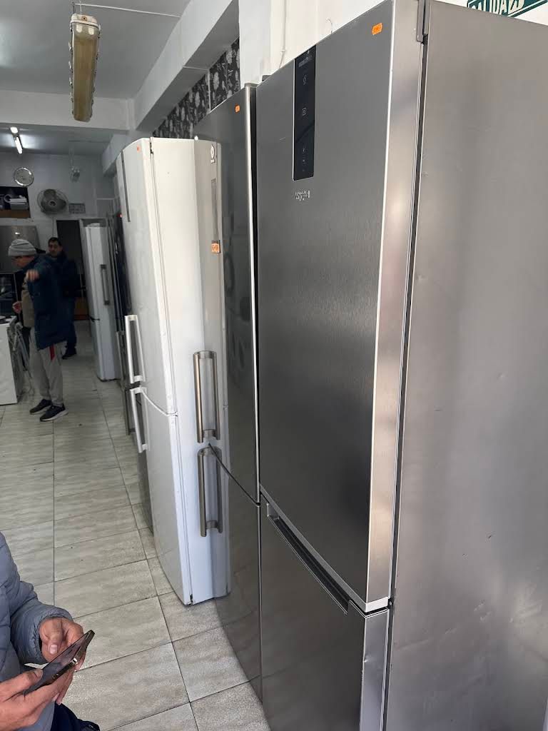 Pasillo estrecho con un frigorífico grande de acero inoxidable y un frigorífico blanco al lado; una persona está de pie al fondo.