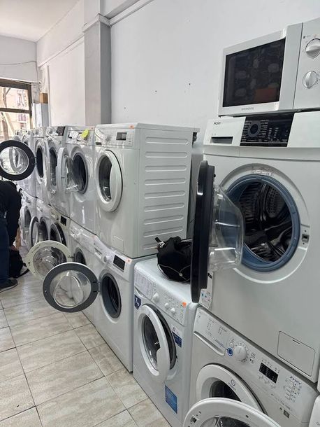 Fila de lavadoras y secadoras blancas en una lavandería con suelo de baldosas y paredes luminosas.